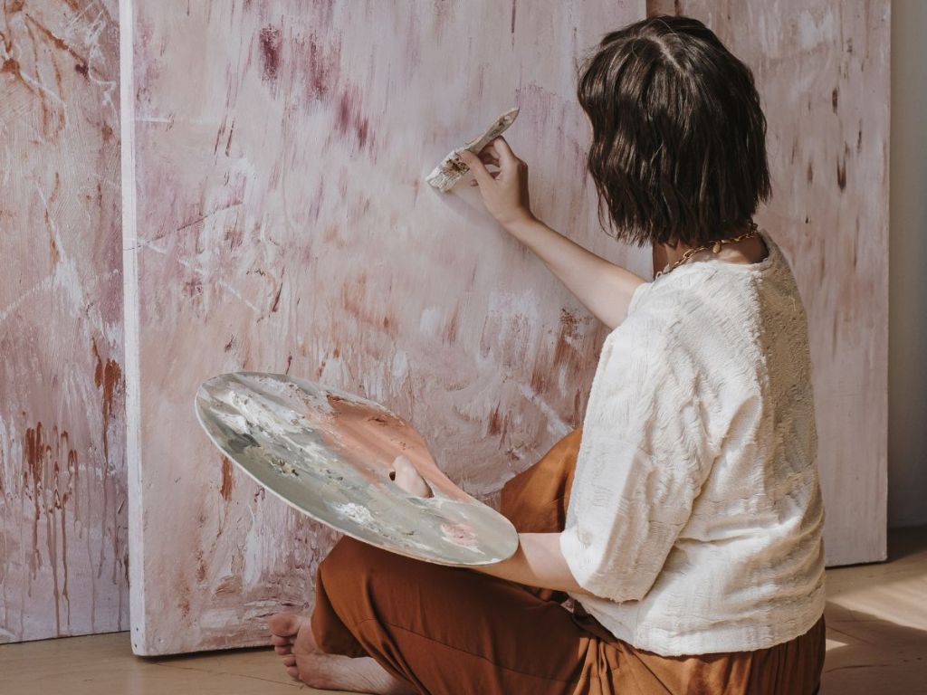 woman sitting on the floor while painting on canvas